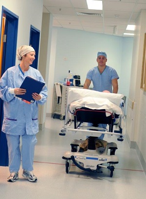 Two clinicial staff pushing a patient in a bed down a hospital corridor
