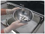 Two gloved hands washing a bowl to ensure clean and sterile reuse of equipment and instruments