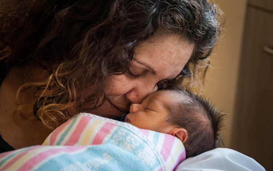 An Aboriginal woman, holding a newborn baby close, nose to nose.