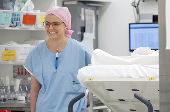 A nurse wearing scrubs, walking with a patient in a hospital bed.