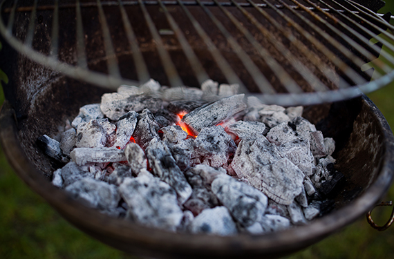Glowing embers in a charcoal barbecue under a grill.