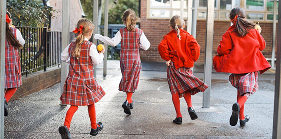 Primary aged girls in uniform, running through a school ground.