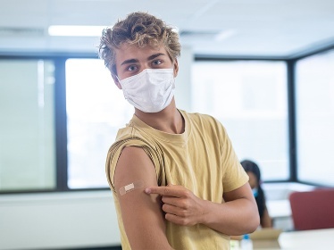 A person with their sleeve rolled up. They are pointing to a band aid on their shoulder.