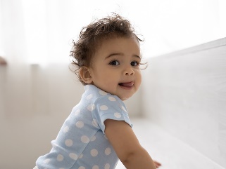 A 12 month old baby leaning up on a seat.