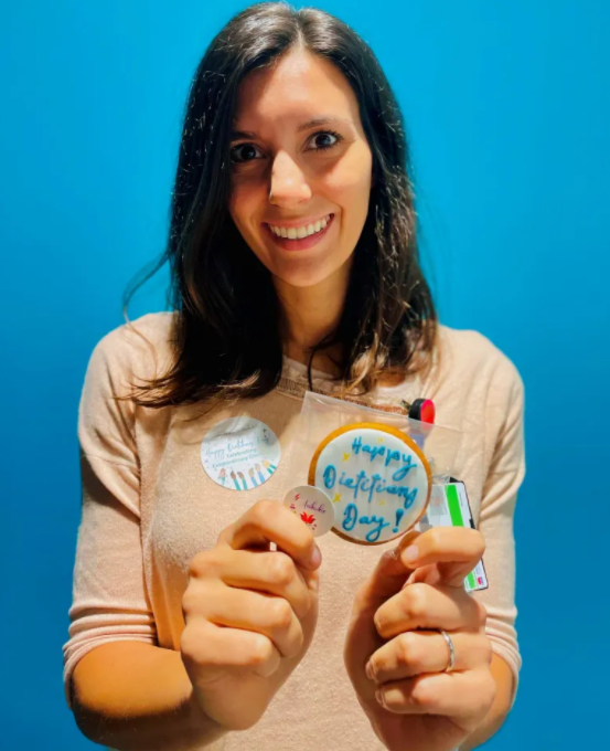 A young brunette woman smiling and holding a cookie frosted with 'Happy Dietician's Day'