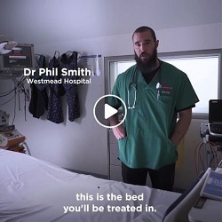 Dr Phil Smith from Westmead Hospital standing next to a hospital bed with subtitle 'This is the bed you'll be treated in'. and play button superimposed