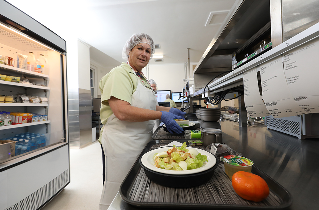 A woman wearing an apron and hair cover prepares food in a kitchen