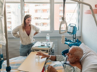 A person visiting an older patient in a hospital room.