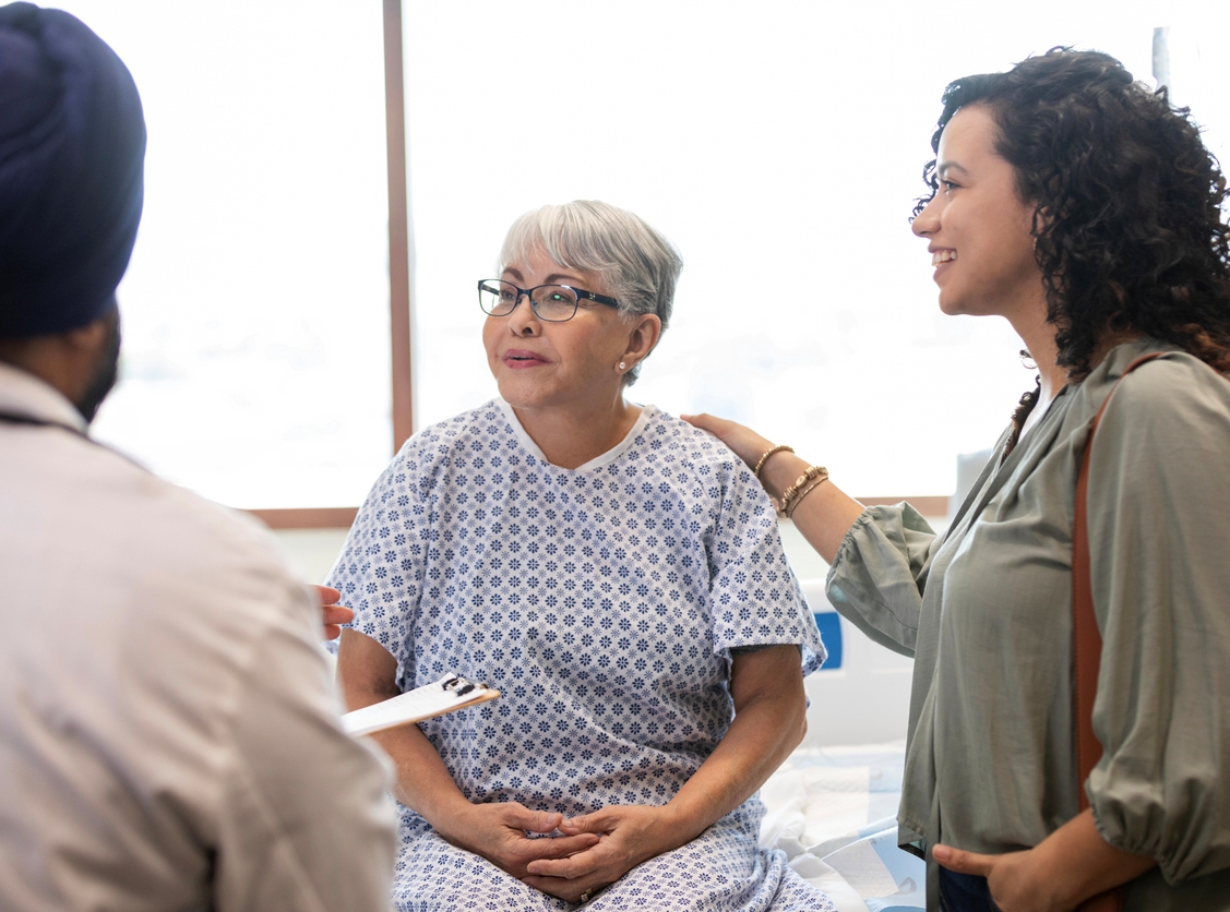 An older person seated next to a carer, with the carer holding and supporting them.