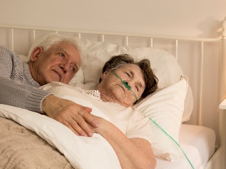 An older couple resting in a hospital bed together.