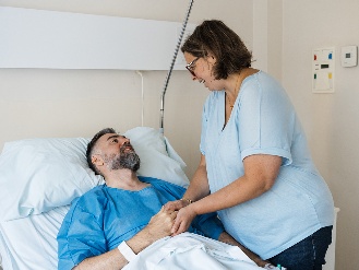 A person supporting another person resting in a hospital bed.