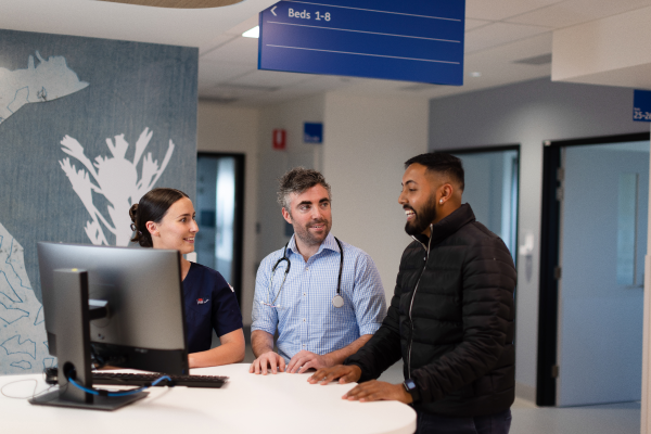 three people are standing in front of a computer in a hospital setting