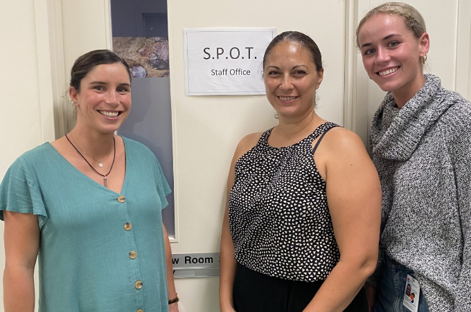 Three women od varying ages all wearing pony tails stand in front of an office door