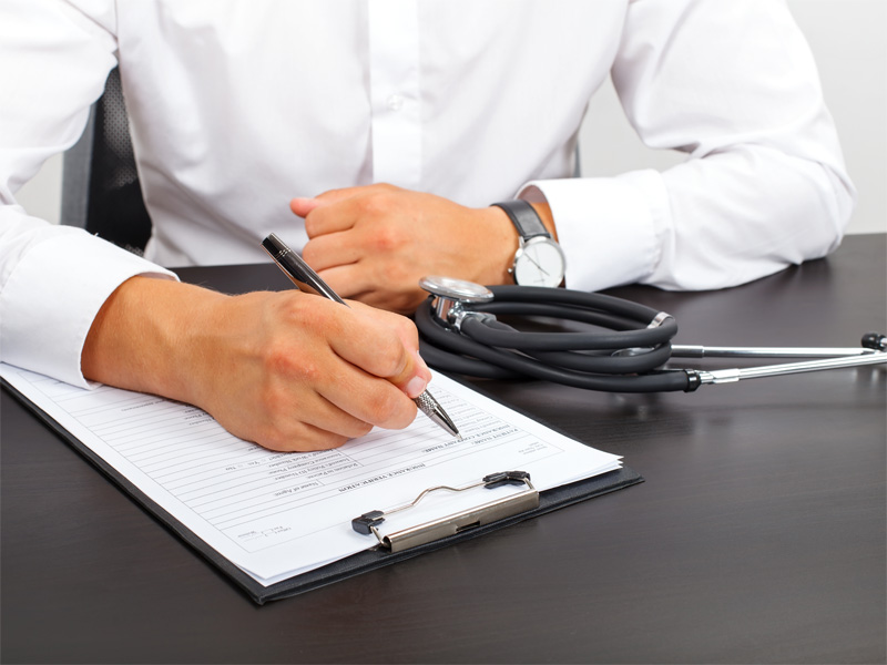 A doctor writing on a clipboard on a desk.