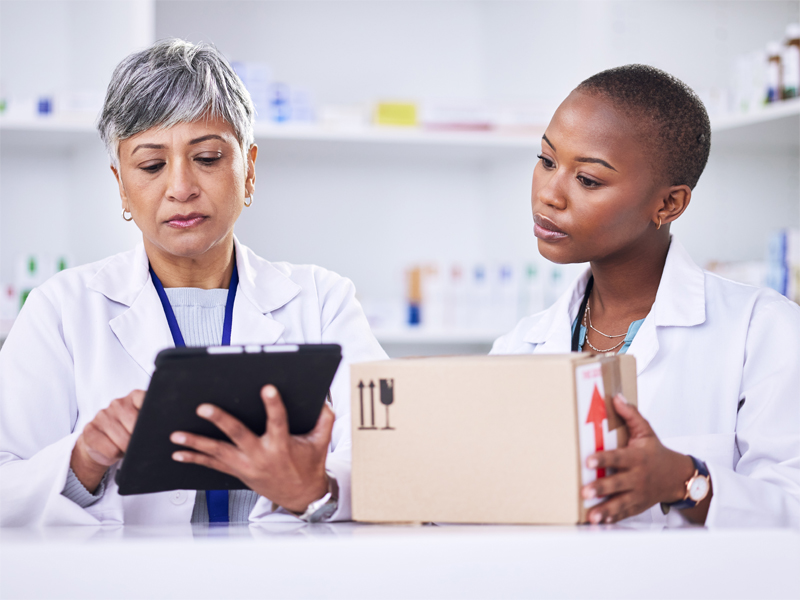 2 pharmacist. One is holding a clipboard and the other is holding a package.