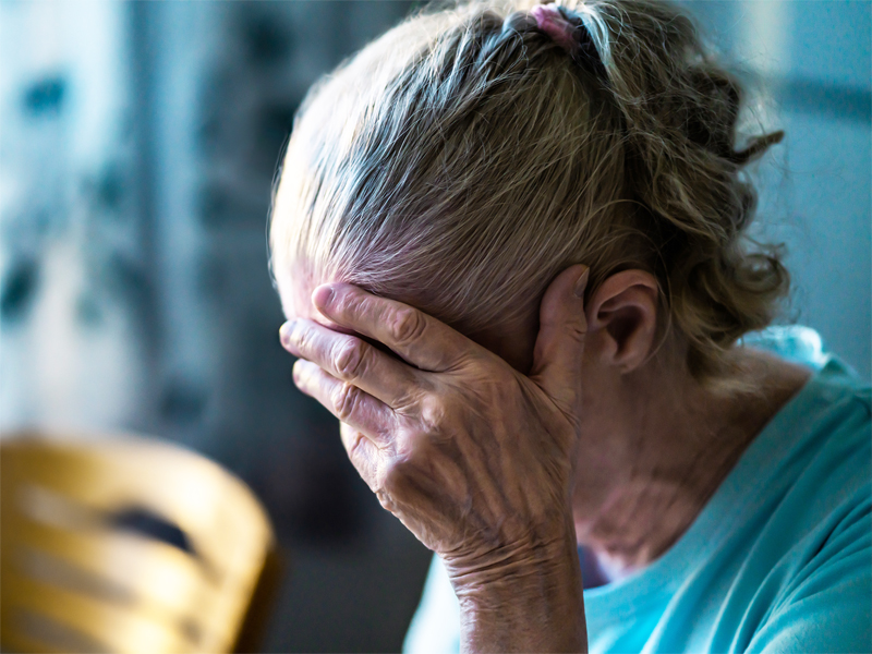 A person with their head faced down. They are covering their face with their hand.