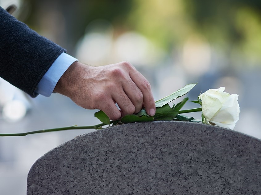 A person placing a flower on top of a gravestone.