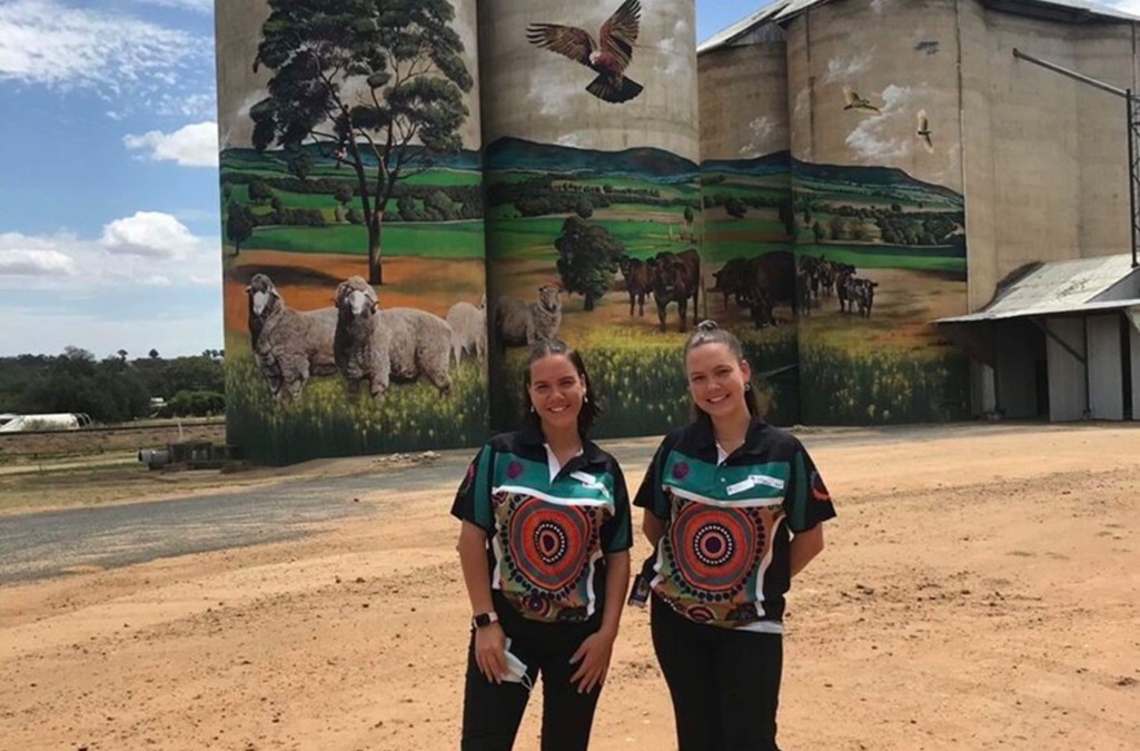Former cadets and sisters, Anna Husband and Lucy Husband standing in front of silos painted with a farming landscape