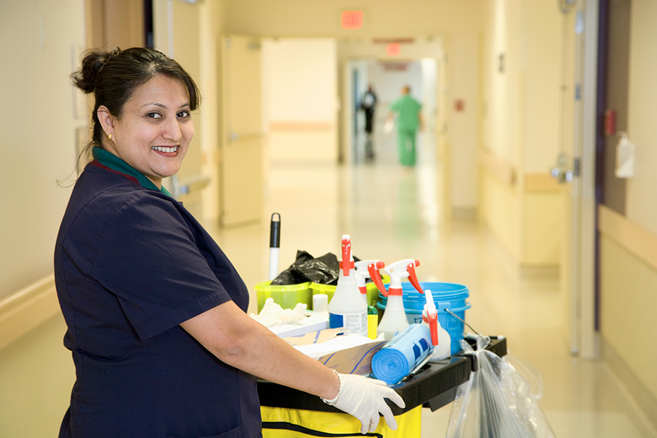 Woman with hands in gloves, holding a trolley full of cleaning supplies