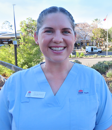 A young woman with dark hair, smiling, wearing light blue NSW Health scrubs.
